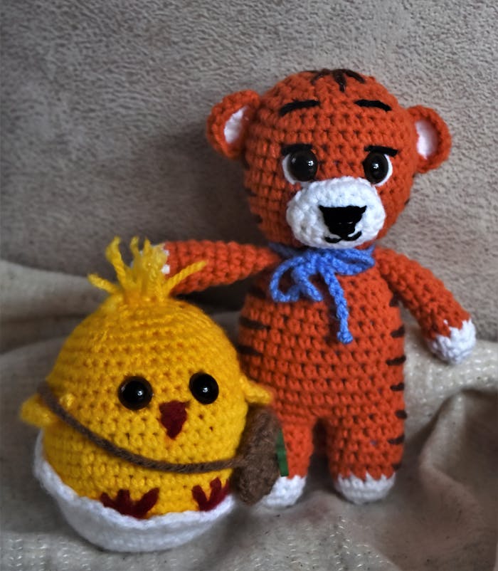 Adorable handmade knitted tiger and chick plush toys on a soft background.