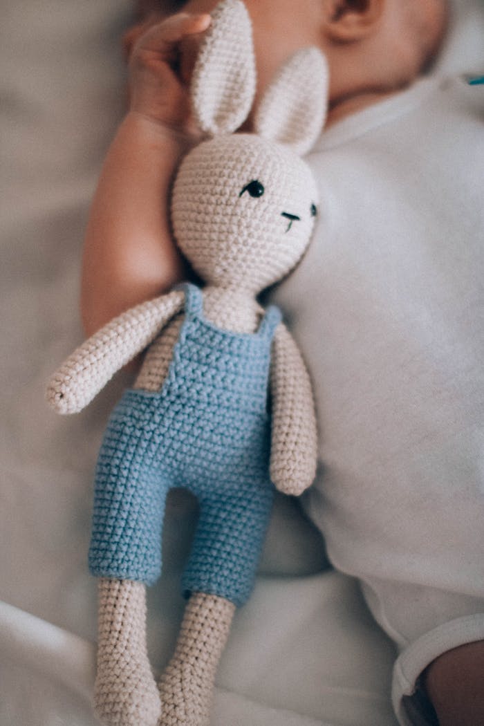 A cute baby lies next to a handmade crochet bunny doll in soft lighting.
